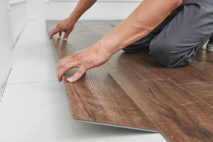 Artisan en tenue orange installe un parquet en lames de bois clair dans une pièce résidentielle
