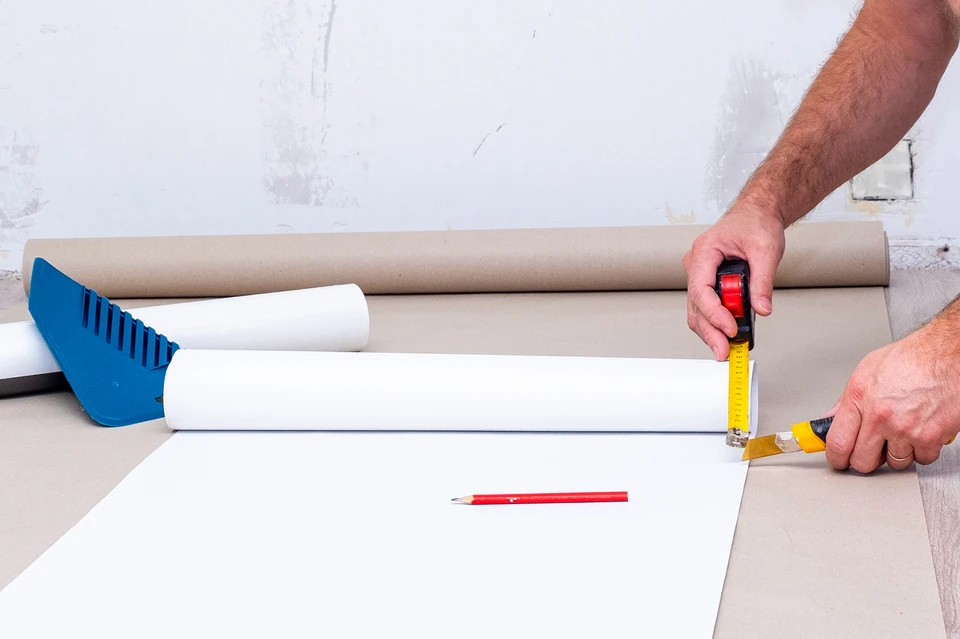 Intérieur d'atelier, artisan appliquant de la colle blanche avec un pistolet à colle sur une planche de bois claire posée sur établi