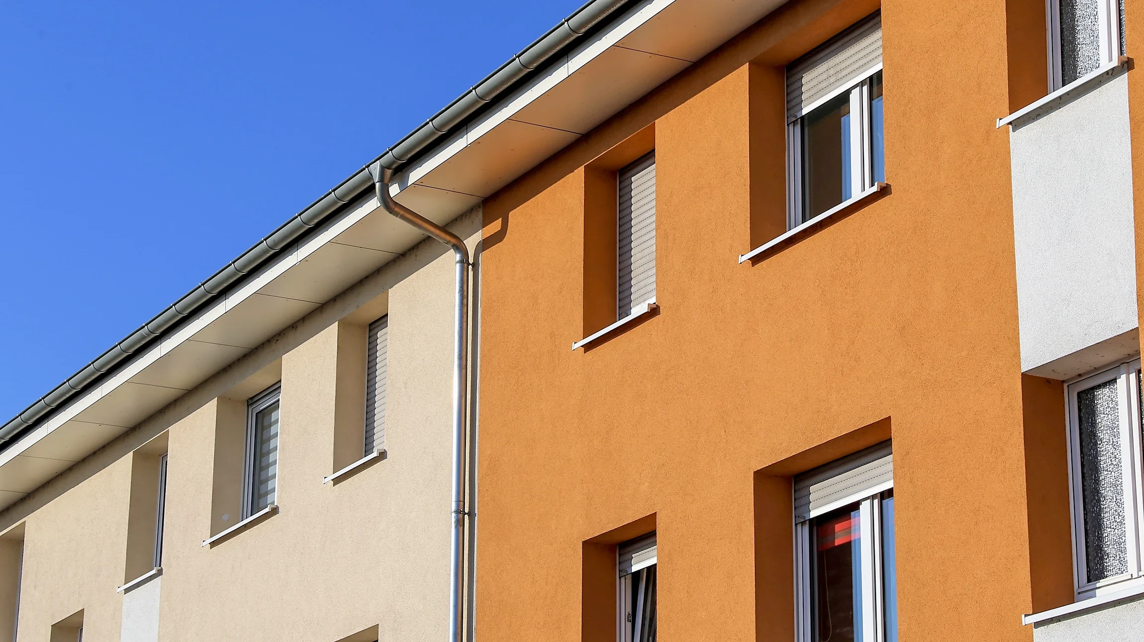 Un peintre en b&acirc;timent sur &eacute;chelle applique de la peinture blanche sur la fa&ccedil;ade ext&eacute;rieure d'une maison