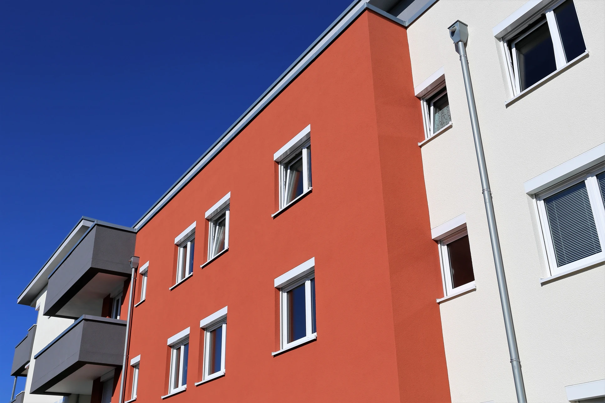 Façade extérieure moderne avec mur en briques peintes vert pâle, porte d'entrée bleue encadrée de blanc, luminaire suspendu doré, plaque d'adresse numérotée, haie verte taillée à la base et trottoir beige